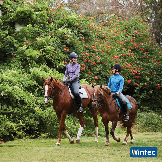 Two riders walking past flowering shrubs on Wintec saddles